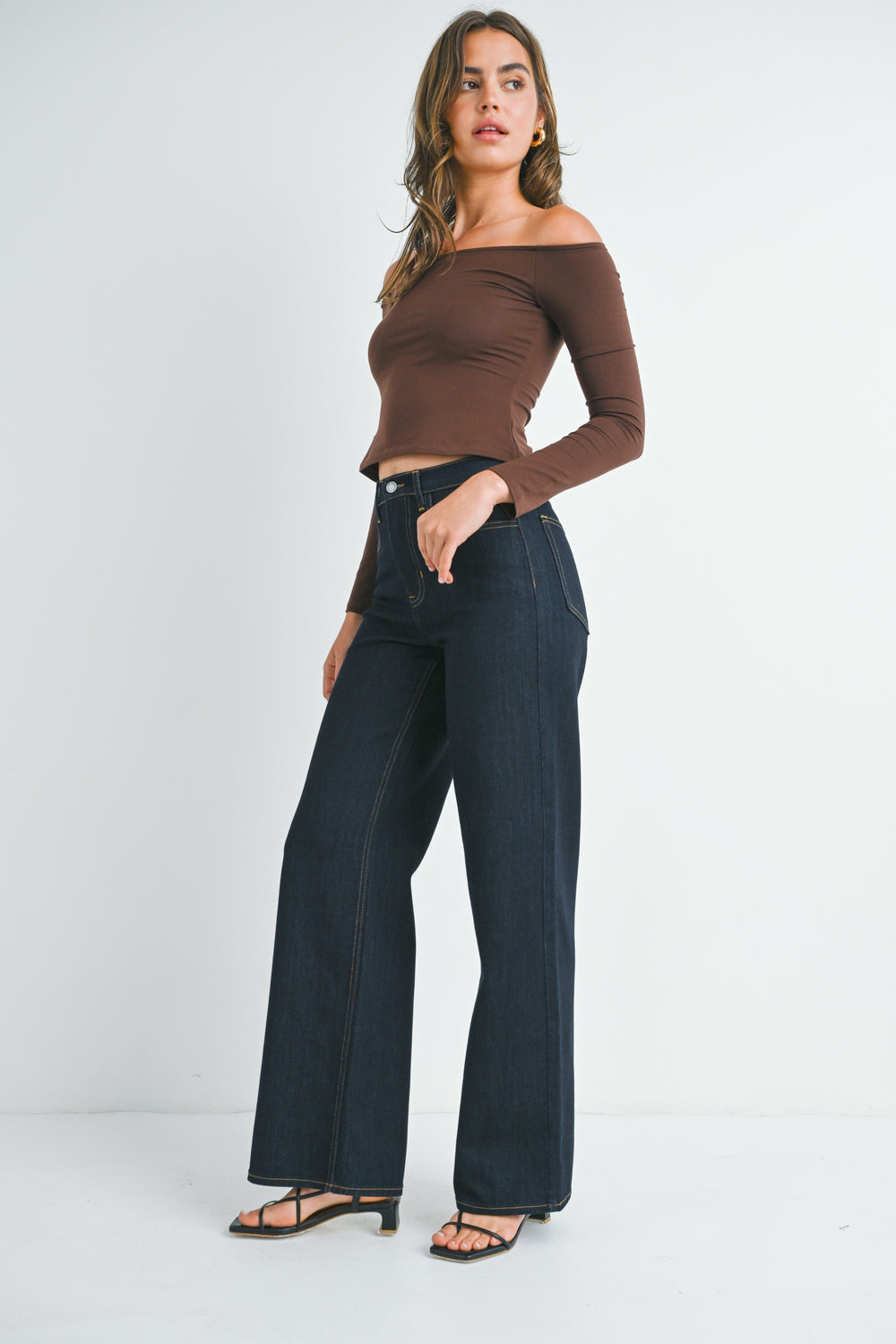 Woman wearing a brown off-shoulder top and dark blue jeans on a white background