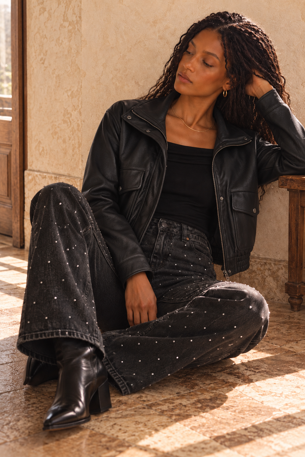 Model wearing a black vegan leather jacket with a black top and embellished jeans