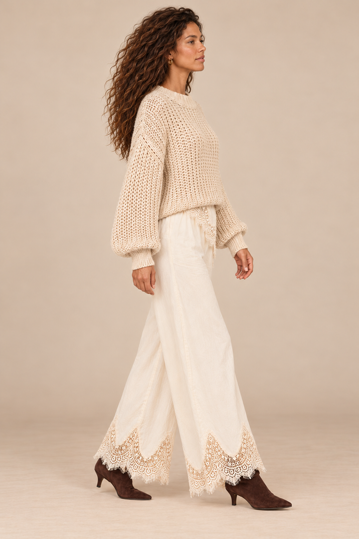 Julia Knit Sweater in Ivory — side view on curly-haired holiday campaign model, cream lace trousers and chocolate boots, light tan studio.
