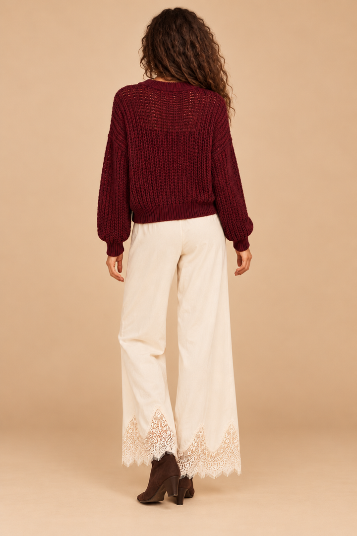 Julia Knit Sweater in Wine — back view on holiday model, cream lace pants and chocolate boots. Light tan studio background.