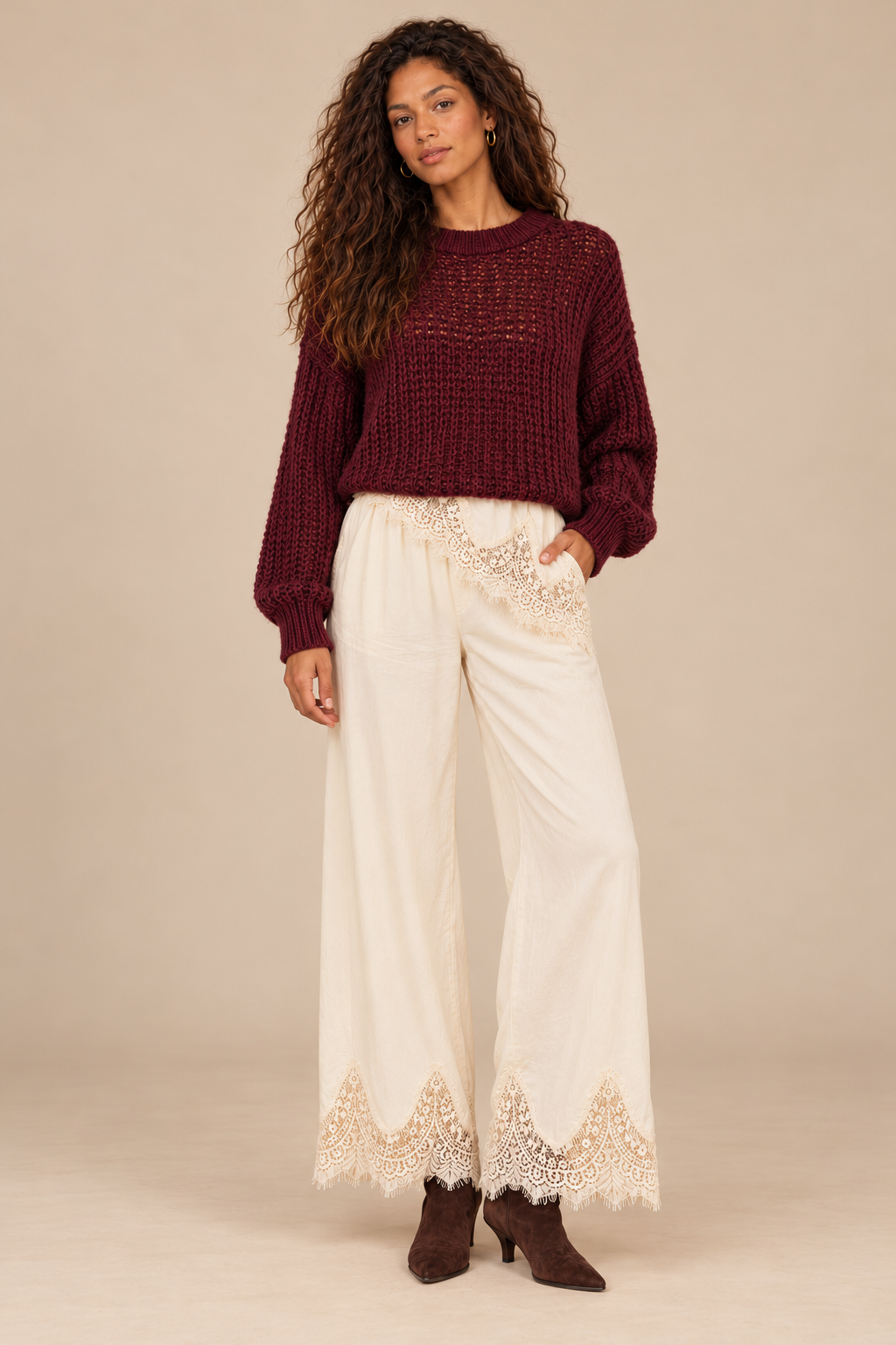 Julia Knit Sweater in Wine — front view on curly-haired holiday model, cream lace-trim pants and chocolate suede boots, light tan studio.