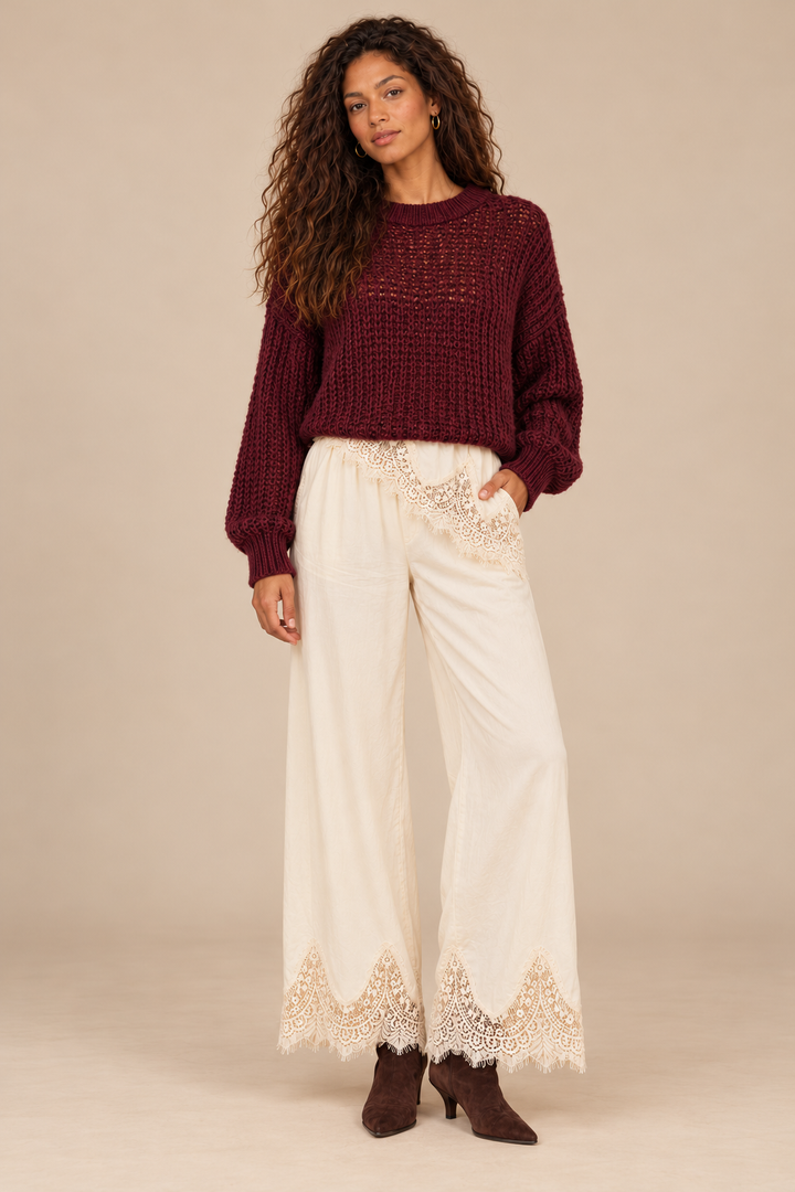 Julia Knit Sweater in Wine — front view on curly-haired holiday model, cream lace-trim pants and chocolate suede boots, light tan studio.