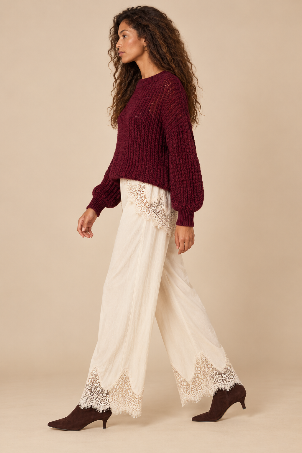 Julia Knit Sweater in Wine — side view on curly-haired holiday model, cream lace-trim pants and chocolate suede boots, light tan studio.