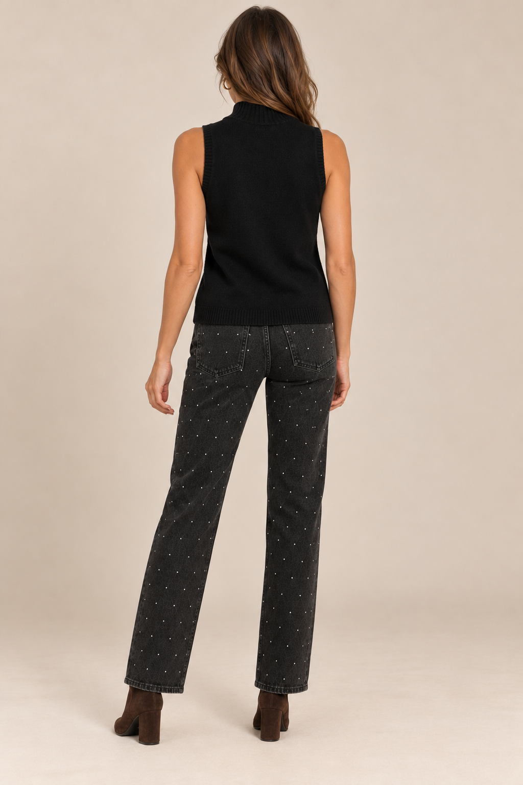 Sleeveless Knit Mock Neck Top in Black — back view on holiday campaign model, rhinestone black jeans and chocolate boots, light tan studio.