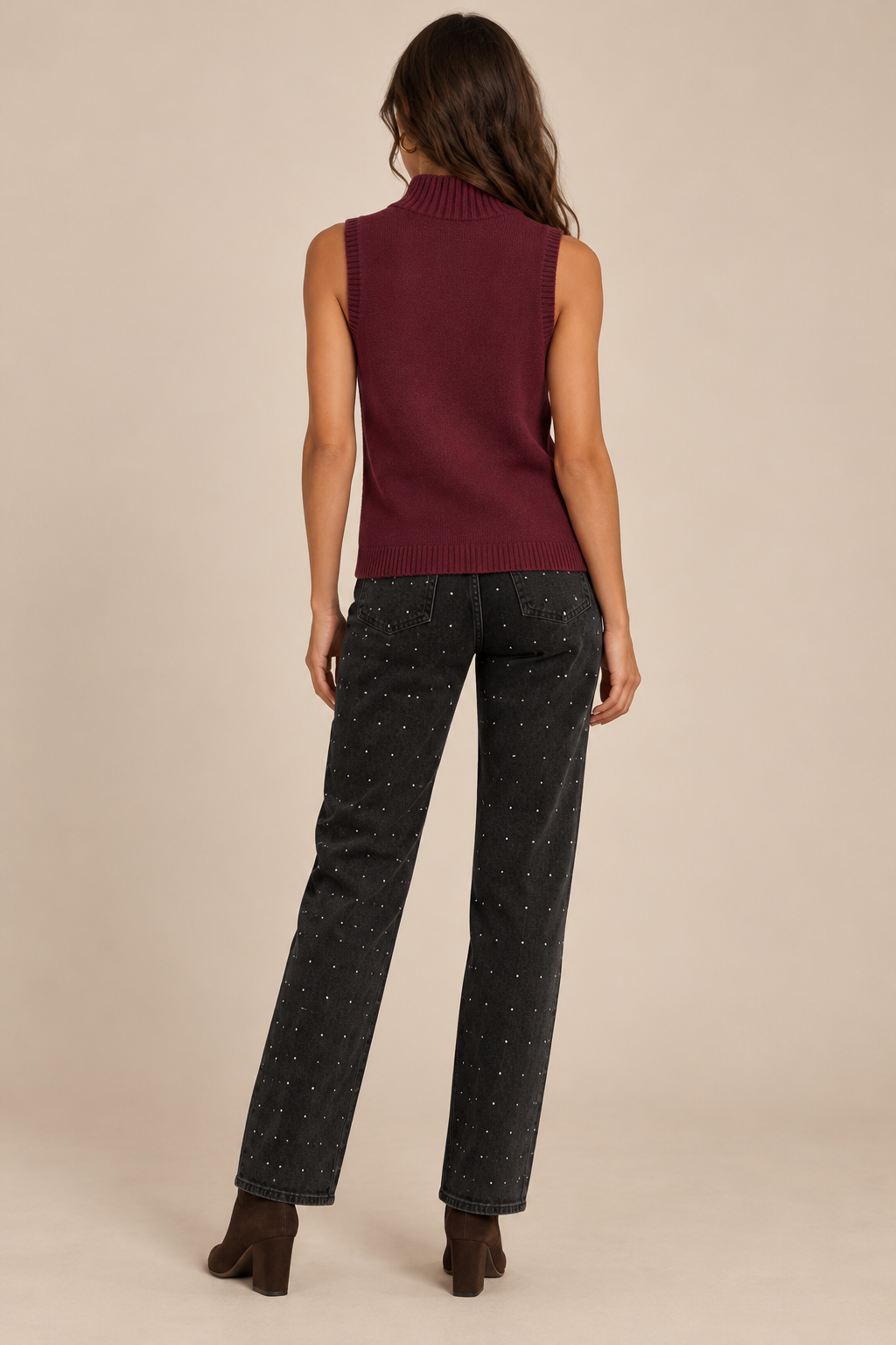 Sleeveless Knit Mock Neck Top in Wine — back view on holiday model, rhinestone black jeans and chocolate boots. Light tan studio background.