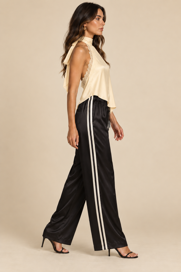 Side Stripe Silky Track Pant in Black Cream — side view on holiday campaign model, styled with satin top and black sandals, light tan studio.