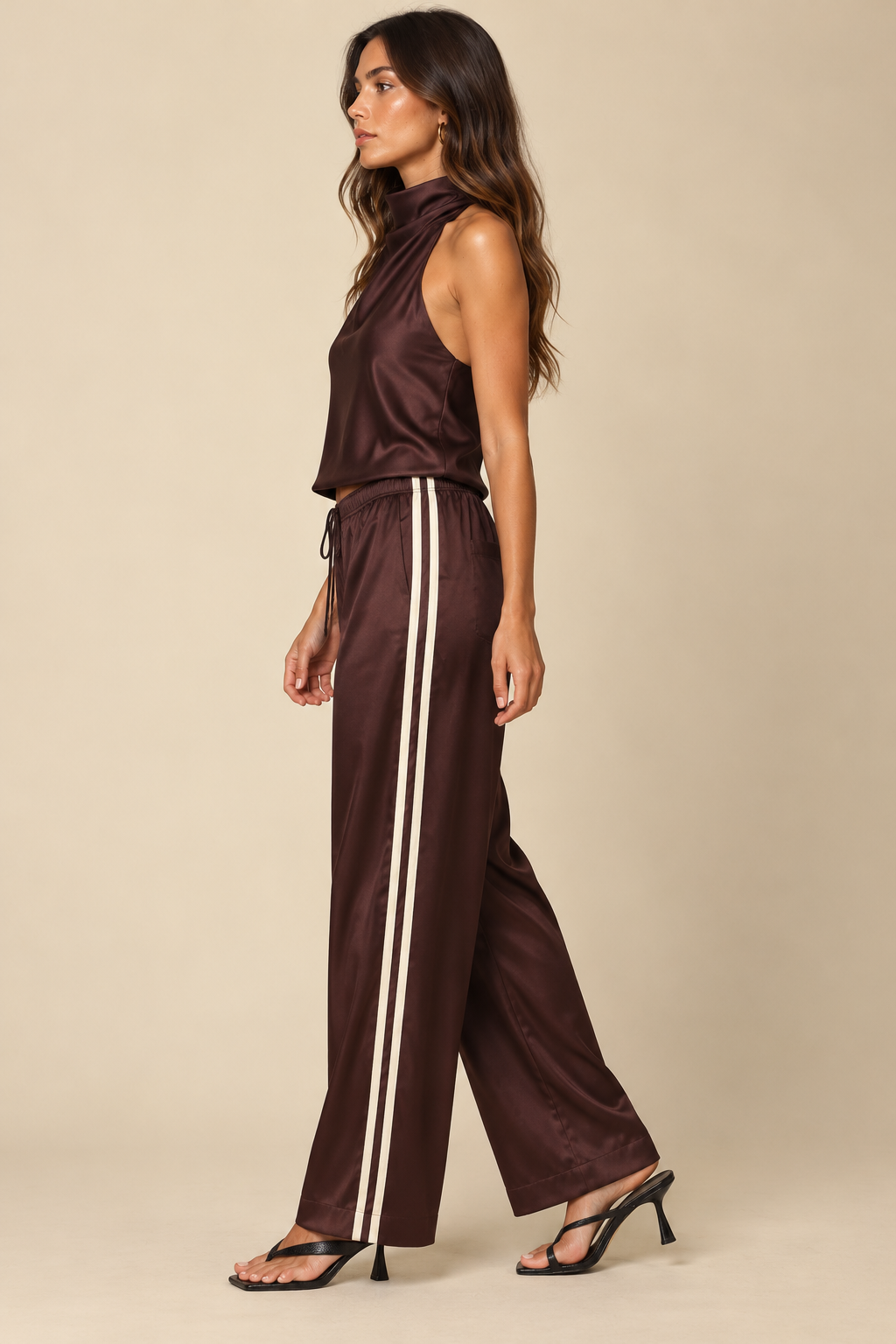 Side Stripe Silky Track Pant in Brown Natural — side view on holiday campaign model, coordinated satin halter and black sandals, light tan studio background.